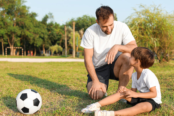 Father and his little son with bruised knee after playing soccer on field - Foto, Imagen