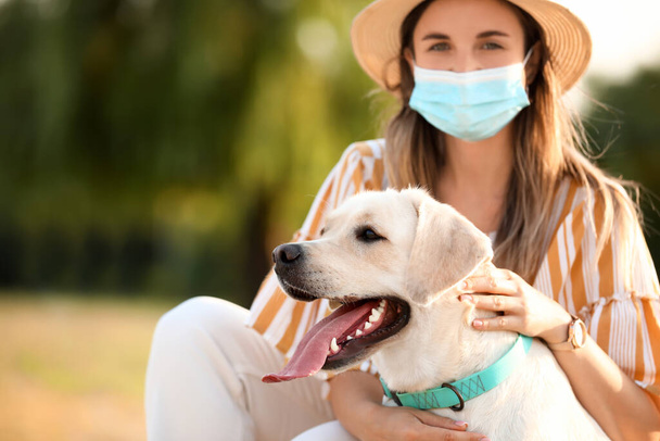 Женщина в медицинской маске и милый лабрадор на открытом воздухе в летний день - Фото, изображение