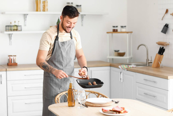 Jonge man met baard zet gebakken worsten op bord in de keuken - Foto, afbeelding