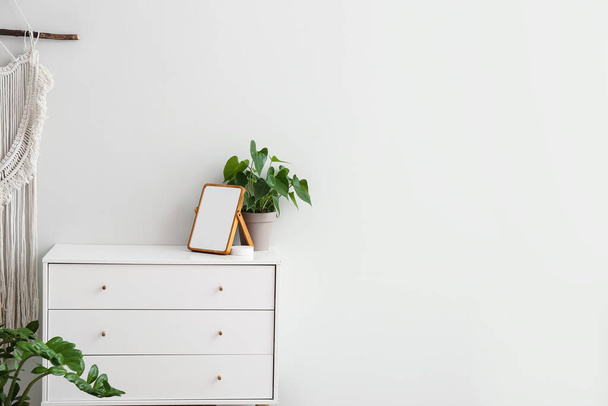Modern chest of drawers, blank frame and houseplants near white wall - 写真・画像