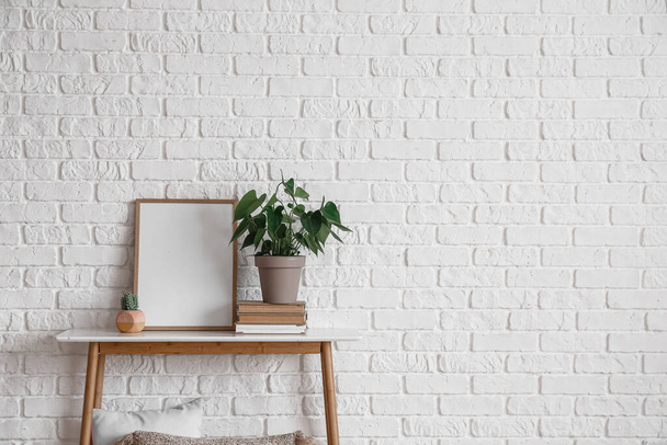 Beautiful houseplant and blank frame on table near white brick wall - Foto, Bild