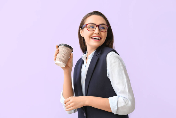 Pretty young businesswoman with cup of coffee on lilac background - 写真・画像