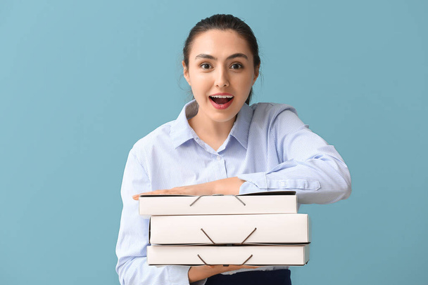Surprised young businesswoman with folders on blue background - Фото, изображение