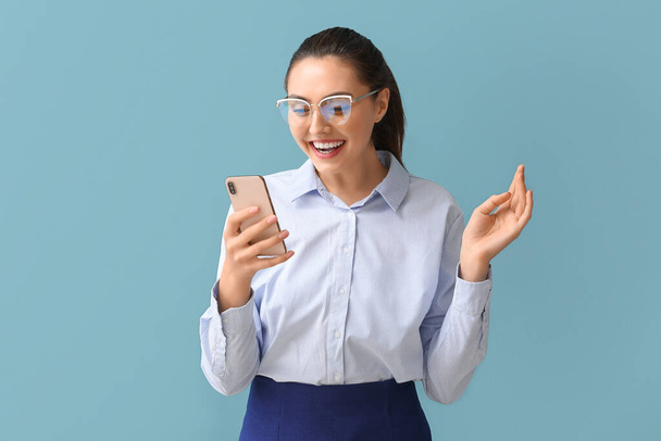 Pretty young businesswoman using mobile phone on blue background - Foto, afbeelding
