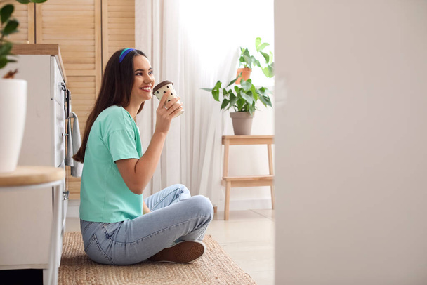 Młoda kobieta pije kawę na podłodze w kuchni - Zdjęcie, obraz