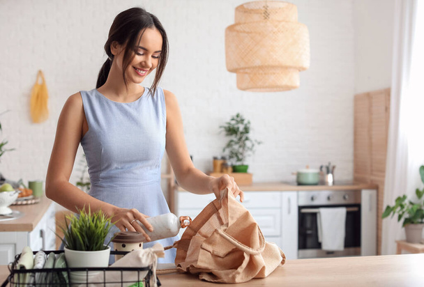 Young woman with bottle and eco bag in kitchen - Foto, Imagen