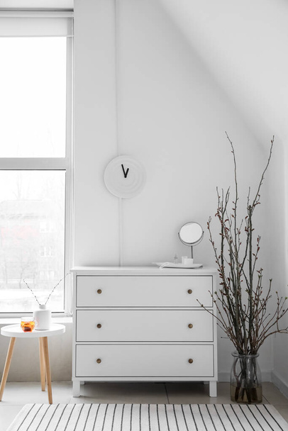 Kommode mit Spiegel, Tisch, Vasen und Ästen im hellen Badezimmer - Foto, Bild
