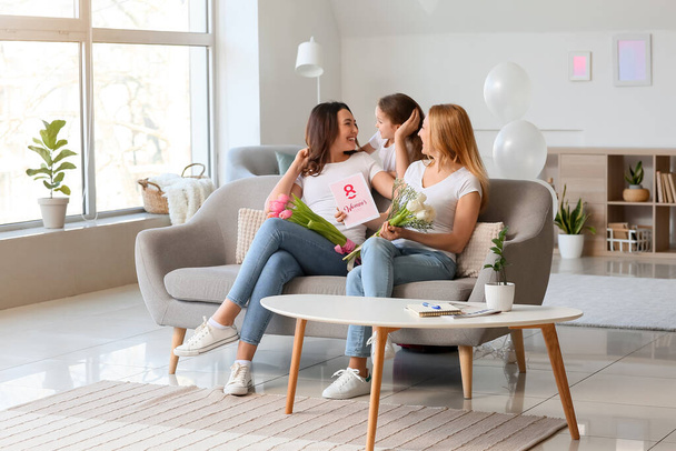 Young woman, her little daughter and mother with flowers and greeting card on International Women's Day at home - Photo, Image