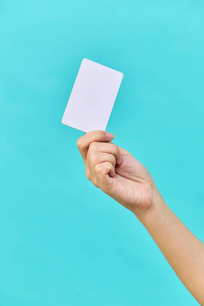 Female hand holding a blank business card on light blue studio isolated background - Photo, image