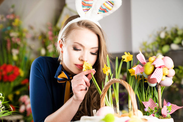 Pretty young women with bunny ears parepaing easter decorations.  Easter background. Bouquets of spring flowers. Easter eggs in baskets. - Фото, изображение
