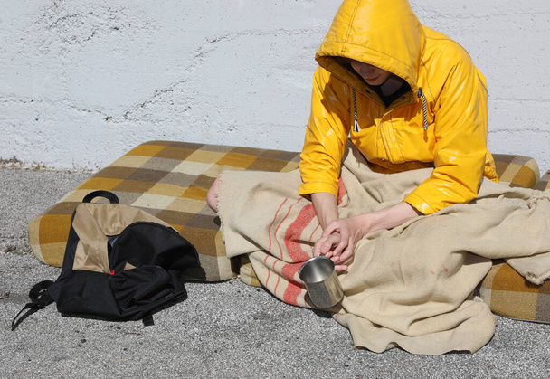 ζητιάνος κάθεται σε ένα βρώμικο στρώμα στο δρόμο ζητώντας φιλανθρωπία και ελεημοσύνη - Φωτογραφία, εικόνα