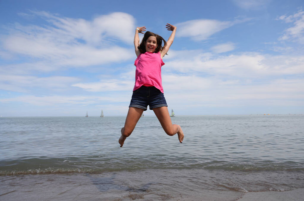 slank jong meisje neemt een zeer hoge sprong en is erg blij door de zee in de zomer - Foto, afbeelding