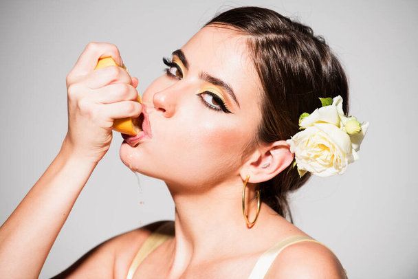 Close up portrait of sexy woman with stylish makeup on beautiful face squeezing juice from fresh orange, lick orange juice on a gray background. - Φωτογραφία, εικόνα