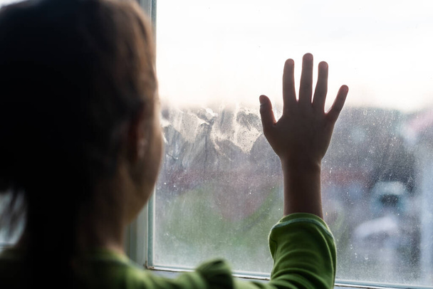 Fiatal lány az ablaknál kezét nyomja az ablakhoz, töprengő vagy akar ki - Fotó, kép