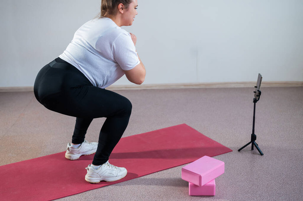 A chubby young woman is watching an online fitness lesson on a mobile phone. Distance sports training - Photo, image