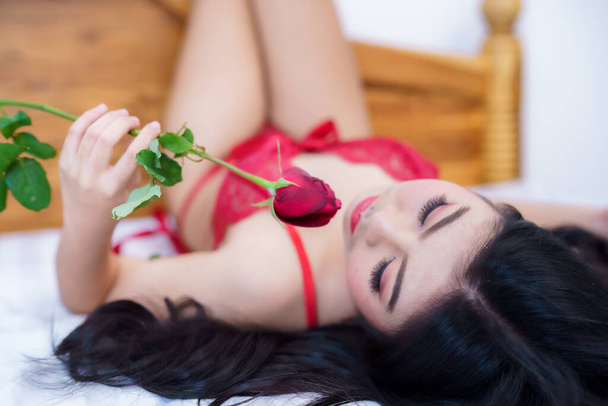 Tanned woman's body,Thailand Asian sexy young woman model in sexy red lingerie holding a red rose posing on the bed in the bedroom ,valentine's day concept - Photo, Image