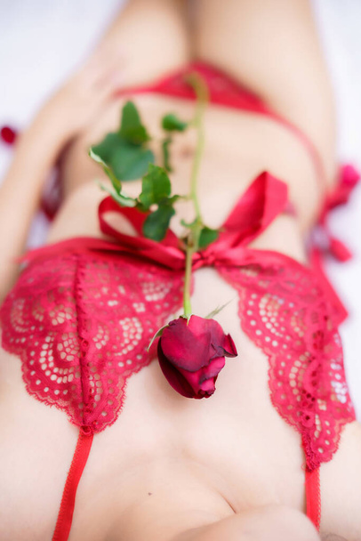 Tanned woman's body,Thailand Asian sexy young woman model in sexy red lingerie holding a red rose posing on the bed in the bedroom ,valentine's day concept - Photo, Image