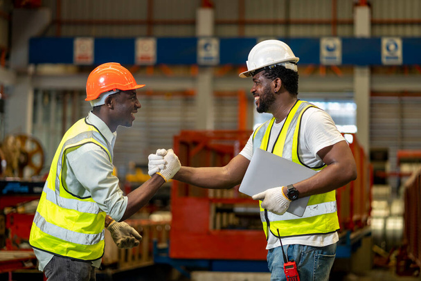 El equipo de trabajadores industriales afroamericanos está estrechando la mano mientras trabaja dentro de la fábrica de techos para la industria de acuerdos y seguridad - Foto, Imagen