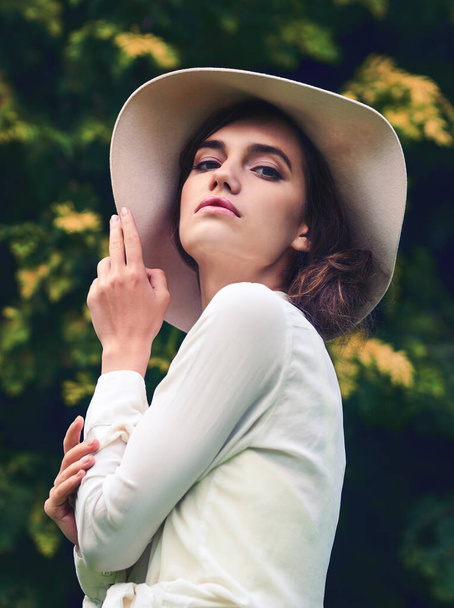 Έχεις δει ποτέ την ομορφιά πιο γοητευτική; Πορτρέτο μιας ελκυστικής νεαρής γυναίκας που φοράει ένα κομψό καπέλο σε εξωτερικούς χώρους. - Φωτογραφία, εικόνα