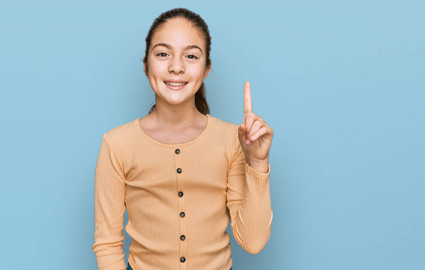 Beautiful brunette little girl wearing casual sweater showing and pointing up with finger number one while smiling confident and happy.  - Foto, Imagem