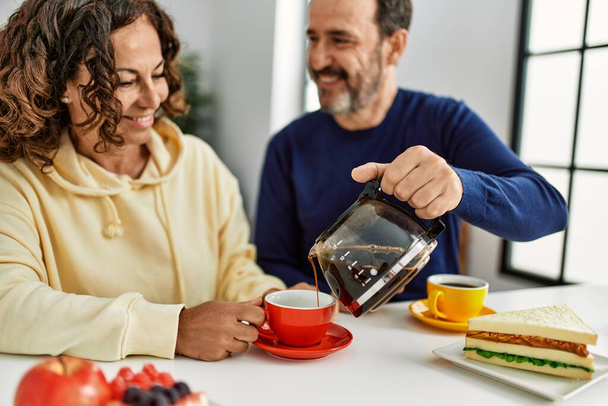 Middle age hispanic couple smiling happy sitting on the table having breakfast at home. - Photo, Image