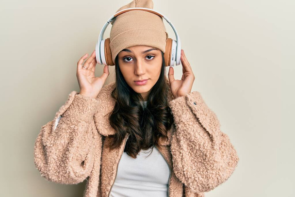 Jeune femme hispanique écoutant de la musique à l'aide d'écouteurs sceptiques et nerveux, fronçant les sourcils bouleversés à cause de problèmes. personne négative.  - Photo, image