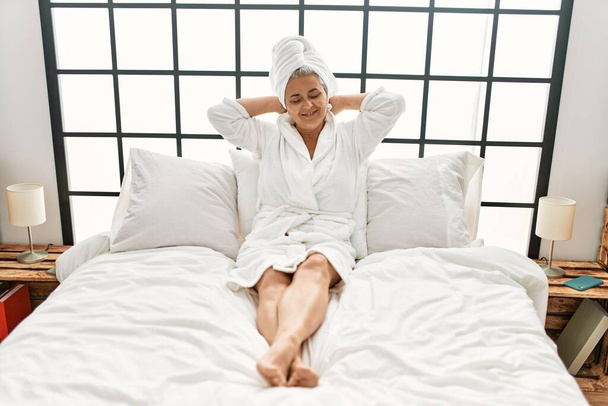 Grauhaarige Frau mittleren Alters lächelnd glücklich auf dem Bett im Schlafzimmer liegend. - Foto, Bild