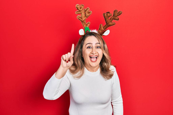 Middle age caucasian woman wearing cute christmas reindeer horns pointing finger up with successful idea. exited and happy. number one.  - Photo, Image