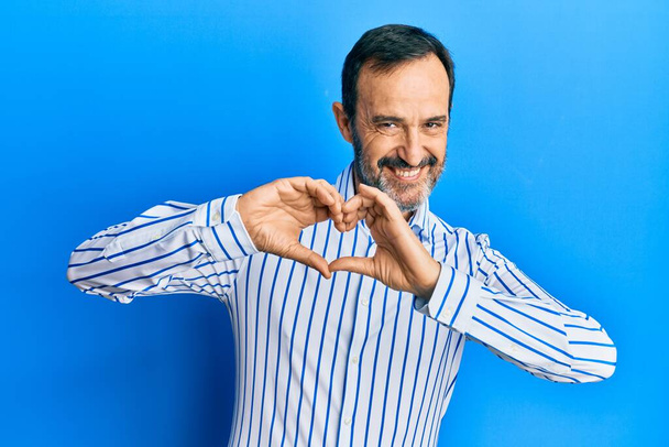 Homme hispanique du Moyen Âge portant des vêtements décontractés souriant dans l'amour faisant forme de symbole de coeur avec les mains. concept romantique.  - Photo, image