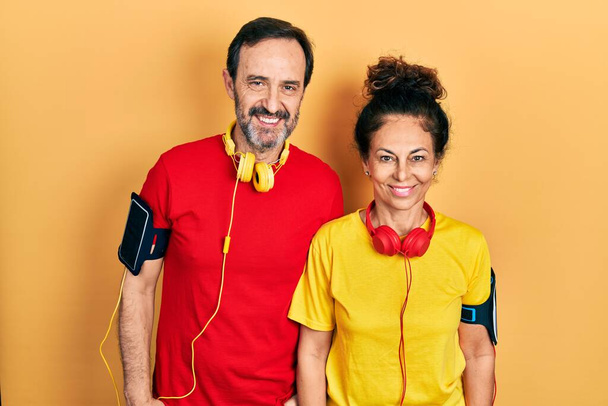 Orta yaşlı bir çift İspanyol kadın ve erkek spor giyer ve yüzünde mutlu ve havalı bir gülümsemeyle kol bandı takar. şanslı kişi.  - Fotoğraf, Görsel