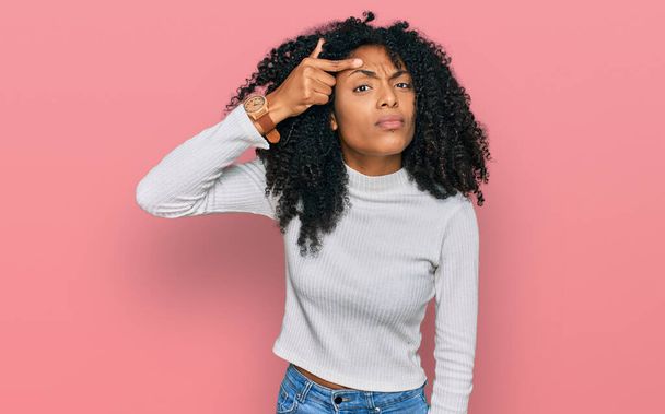 Chica afroamericana joven con ropa casual señalando infeliz a grano en la frente, fea infección de la espinilla. acné y problemas de piel  - Foto, imagen