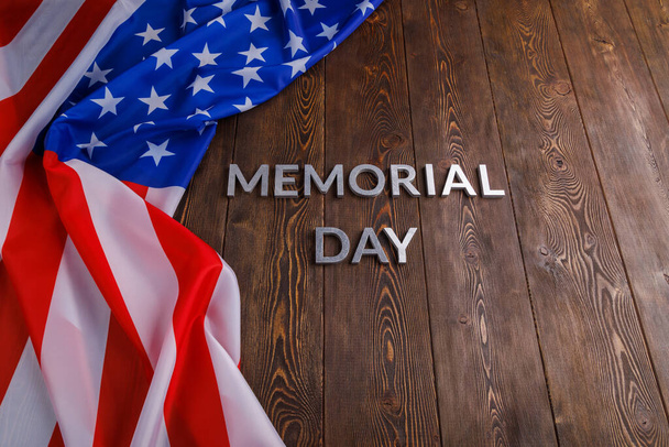 the words memorial day laid with silver metal letters on wooden board surface with crumpled usa flag - Foto, afbeelding