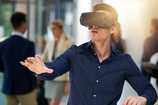 Immergé dans un monde virtuel. Tournage d'un jeune homme d'affaires portant un casque VR dans un bureau occupé. - Photo, image