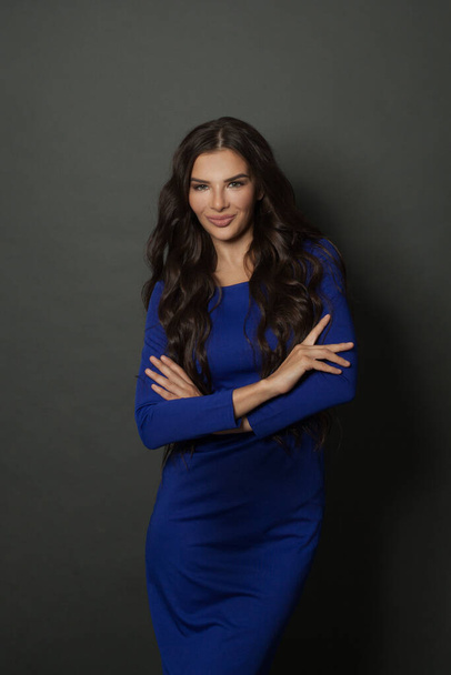 Beautiful young brunette woman with crossed arms. Lady in blue dress on dark gray background - Valokuva, kuva