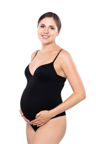 Young pregnant woman in black swimsuit. Girl expecting a baby and touching her belly isolated on white background. - Фото, изображение