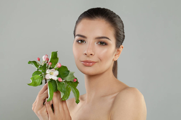 Mooie jonge vrouw met delicate lente bloemen op grijze studio achtergrond - Foto, afbeelding
