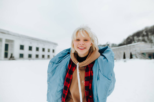 暖かい服を着た幸せなティーンの女の子は雪の通りに立って、彼の顔に笑顔でカメラを見て. - 写真・画像