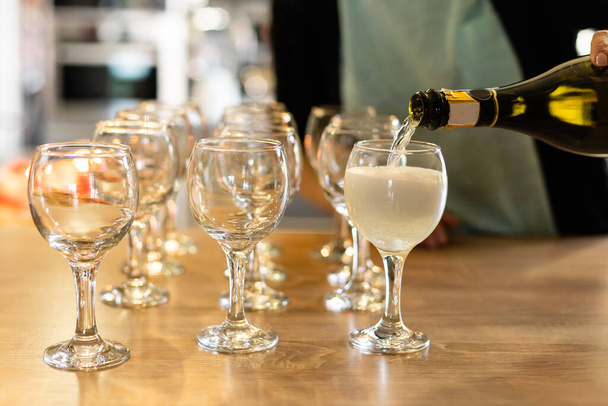 Versare il vino bianco dalla bottiglia nel bicchiere da vino sul tavolo su sfondo sfocato
 - Foto, immagini
