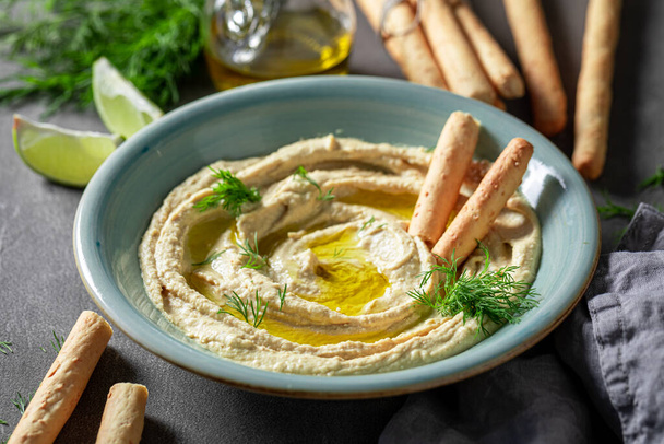 Tasty and homemade hummus with breadsticks, olive oil and dill. Hummus served with breadsticks and olive oil. - Фото, изображение