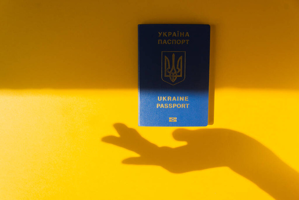 Azul Ucrania pasaporte biométrico en el fondo amarillo energizante con la silueta de una mano de mujer. Inmigración. - Foto, Imagen
