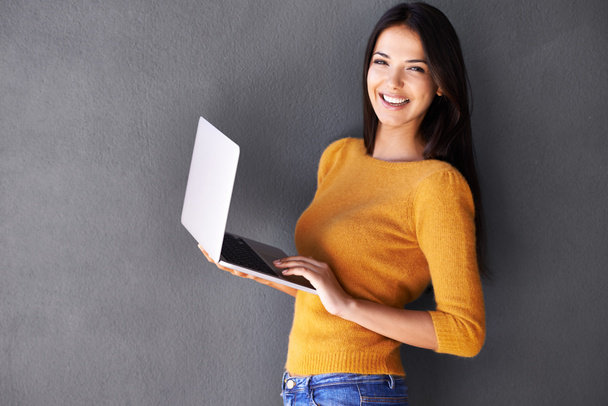 Jest internetowym motylem towarzyskim. Portret pięknej młodej kobiety korzystającej z laptopa na szarym tle. - Zdjęcie, obraz