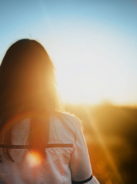 Розмита жінка у вишитій сорочці стоїть з нею назад до заходу сонця
.  - Фото, зображення