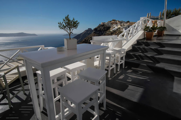 Zapierający dech w piersiach widok z baru na świeżym powietrzu z krzesłami i stołami w Fira Santorini - Zdjęcie, obraz