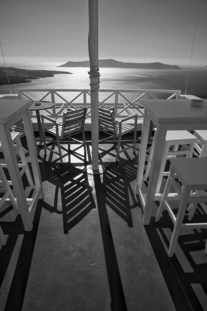 Impresionante vista desde un bar al aire libre con sillas y mesas en Fira Santorini en blanco y negro - Foto, imagen