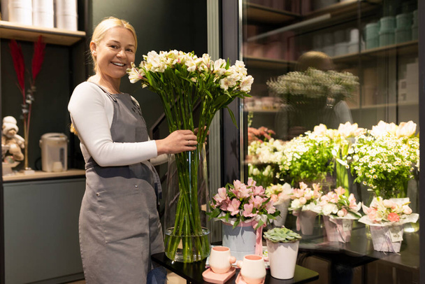 impiegato negozio di fiori accanto a un frigorifero con fiori freschi per mazzi di fiori - Foto, immagini