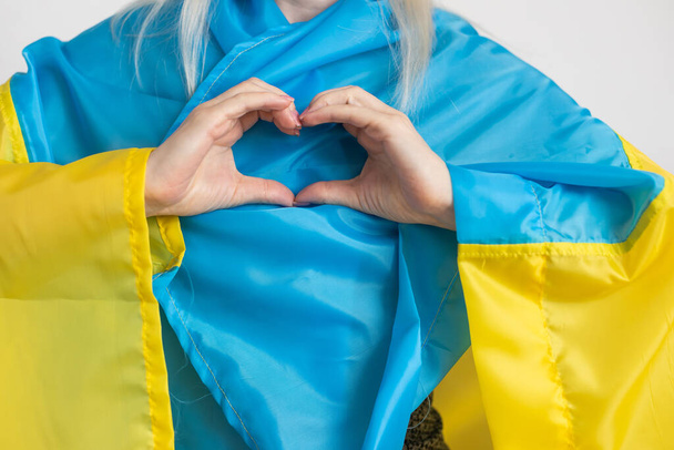 Ukrayna 'daki savaşı bitirme kavramı. Ukrayna bayrağının renginde bir kalp Kadın ellerinde. - Fotoğraf, Görsel