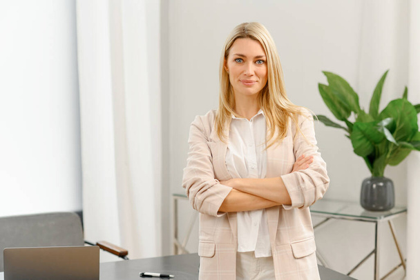 Cheerful young caucasian woman with blonde hairstyle standing in contemporary office, looking at the camera - Foto, afbeelding