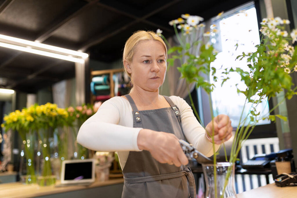 uma florista em uma loja de flores cuida de um buquê, alterando a água e aparando as pontas das plantas - Foto, Imagem