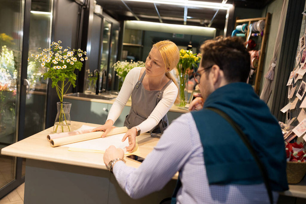 o vendedor e o comprador no interior de uma loja de flores elegante escolhem um pacote para um buquê de margaridas - Foto, Imagem