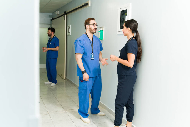 Ελκυστικός γιατρός μιλάει σε χειρουργό στο διάδρομο του νοσοκομείου. Ιατρική ομάδα μιλώντας για έναν ασθενή  - Φωτογραφία, εικόνα